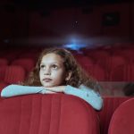 Little girl with curly hair in cinema watching movie
