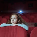Little girl with curly hair in cinema watching movie